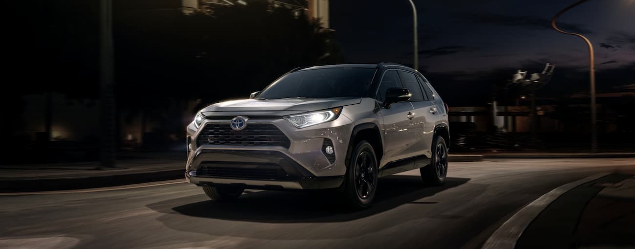 A silver 2020 Toyota RAV4 is driving on a city street at night.