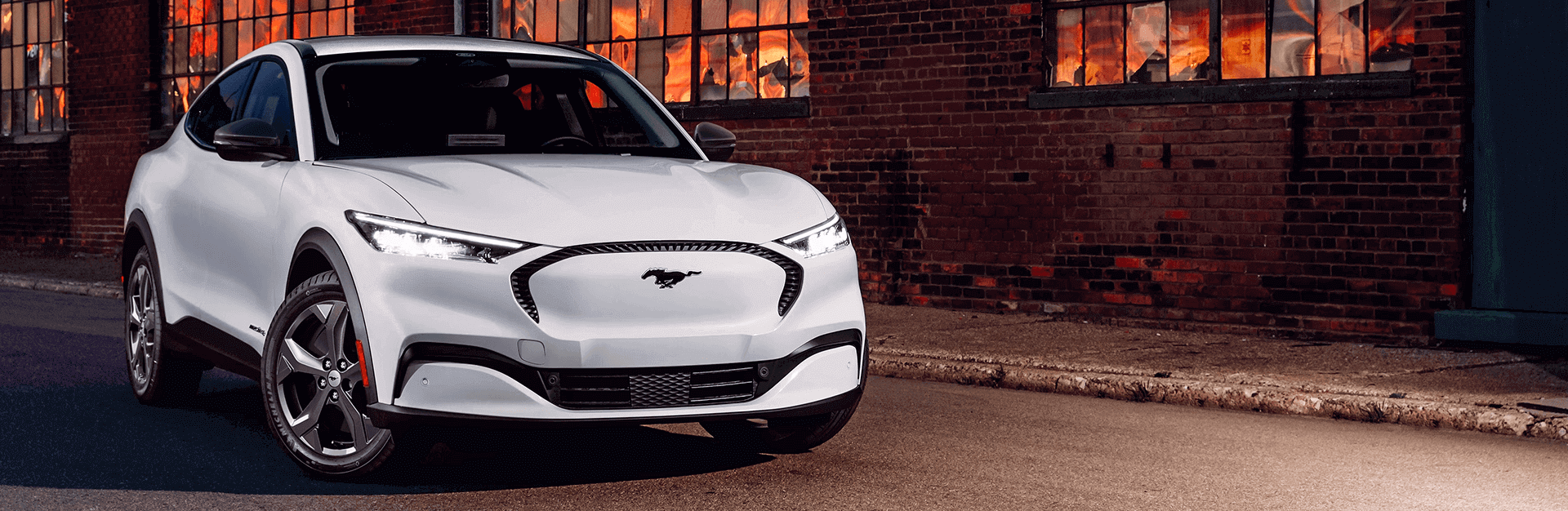White 2024 Ford Mustang Mach-E in parked in front of brig building.