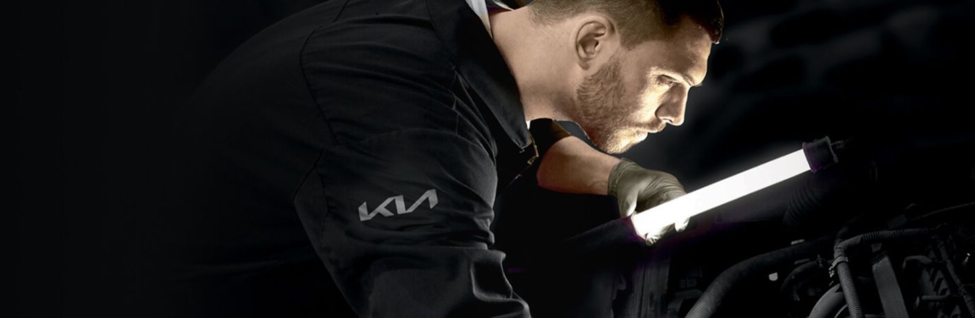 a Kia technician holding a light to look under the hood