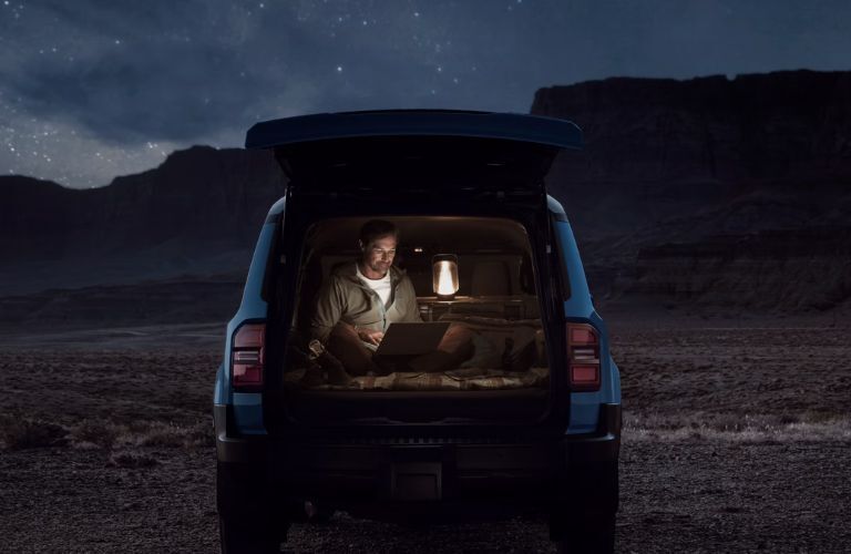 Man sitting in the cargo space of the 2024 Toyota Land Cruiser and working in the lamp light against the backdrop of the mountains