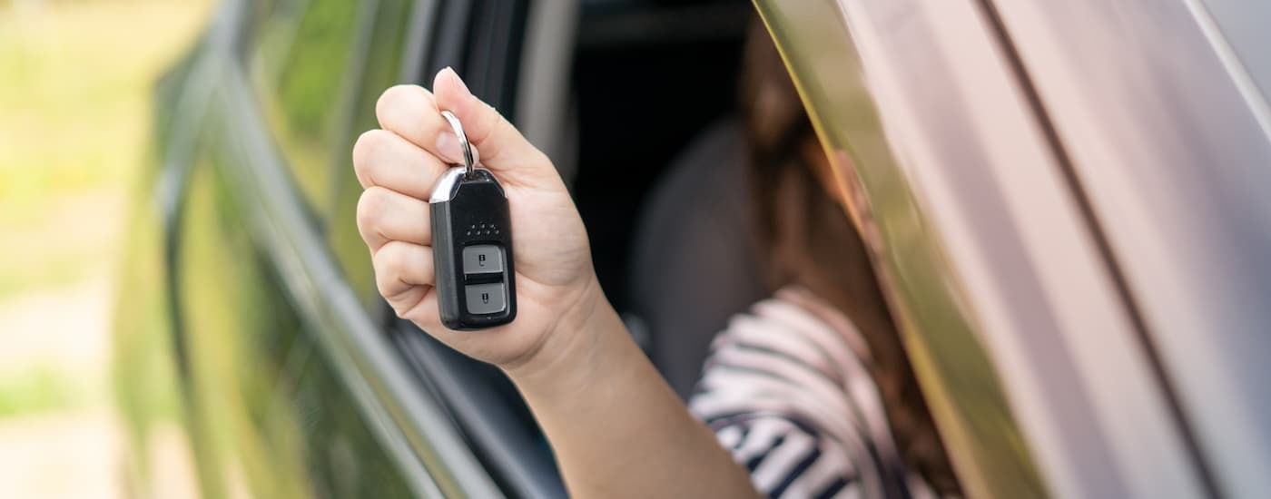 Hand holding out car keys of a used SUV for sale at a dealership.