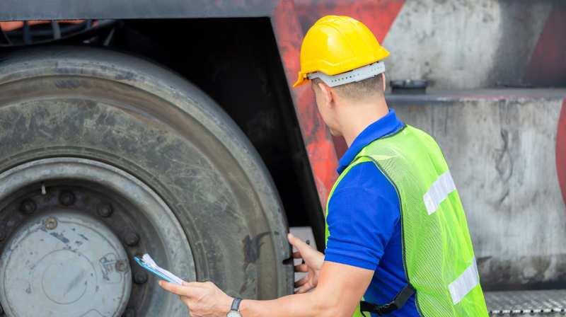 A man inspecting the tires on a heavy garbage truck.