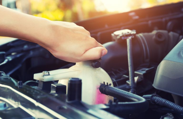 A woman's hand checking the coolant level in a vehicle's engine
