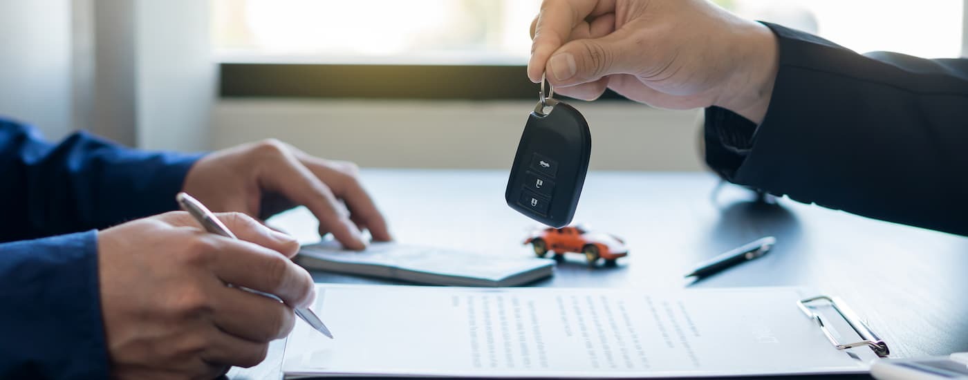 A close up of a salesman handing a key to a customer after they bought a car.