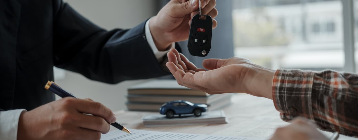 A salesman is handing a car key to a customer inside of a dealership.