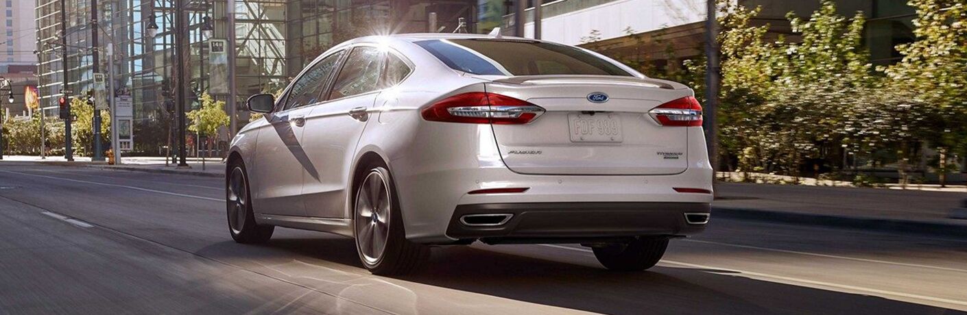 Rear shot of white 2019 Ford Fusion driving on tree-lined city road