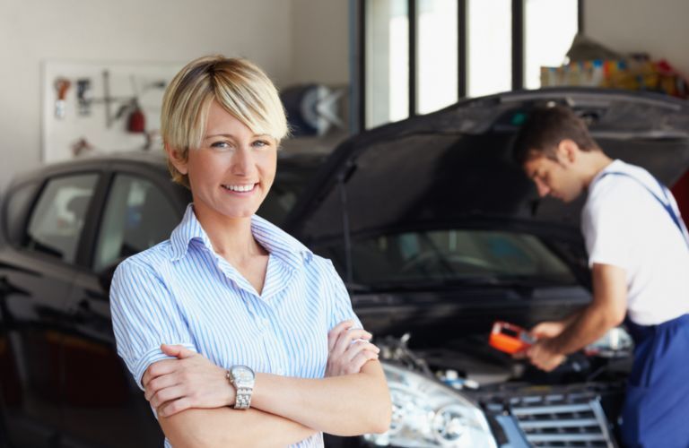 Woman posing with a mechanic working in the background