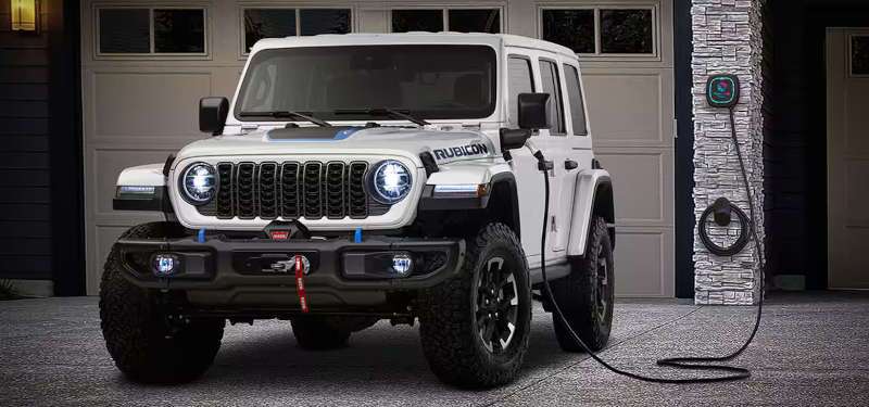 A front exterior view of the 2025 Jeep Wrangler 4xe at a home charging station