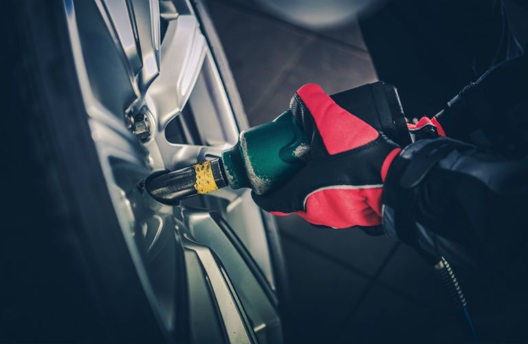 auto technician tightening nuts on tire with tool close up
