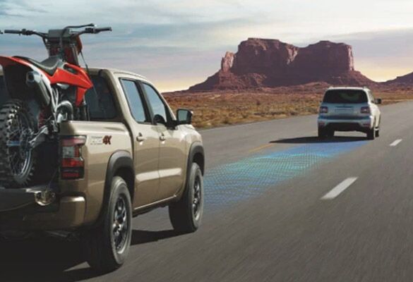 2023 Nissan Frontier with two sports bikes in the bed driving down a highway.