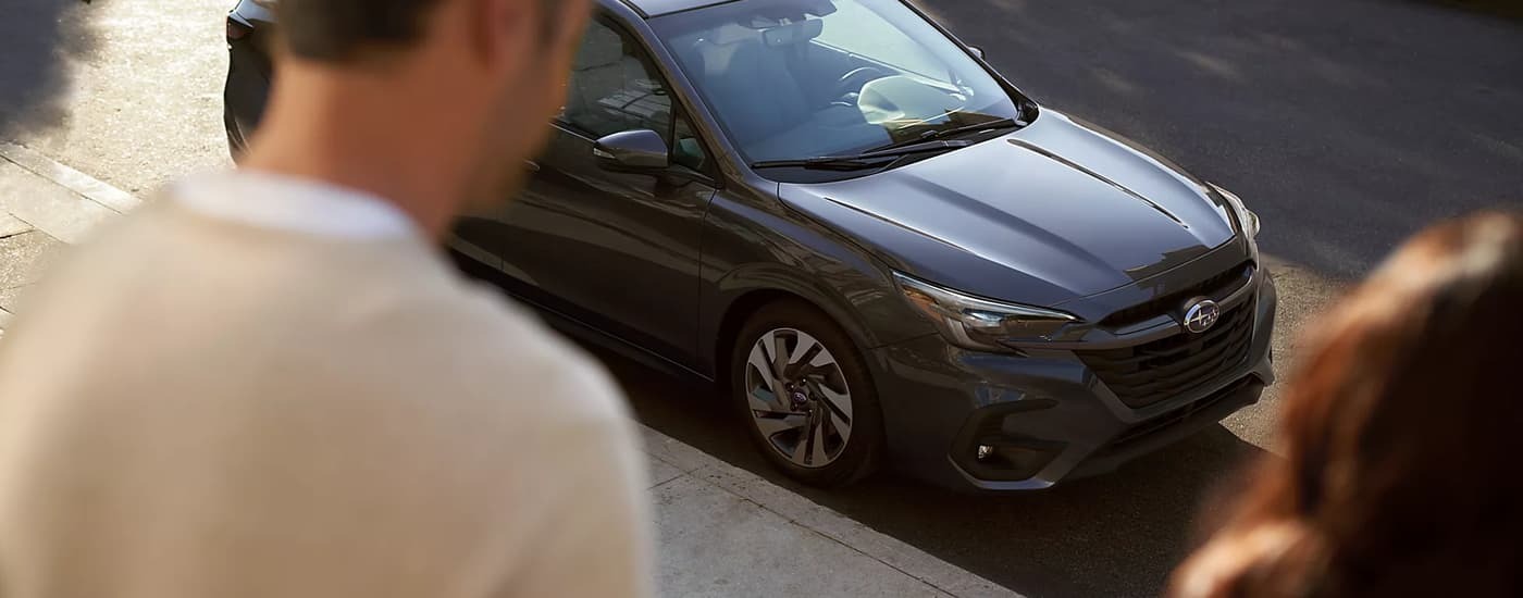 Two people walking near a parked grey 2023 Subaru Legacy near a used car dealership near Hoboken