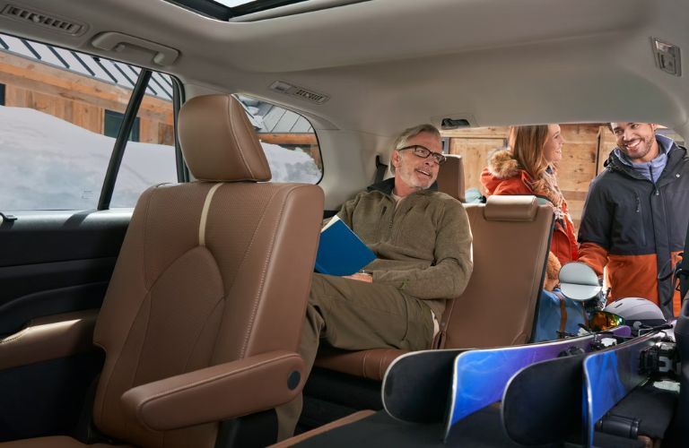 Man sitting in the spacious third row of the 2025 Toyota Grand Highlander while a couple loads up the SUV with their luggage