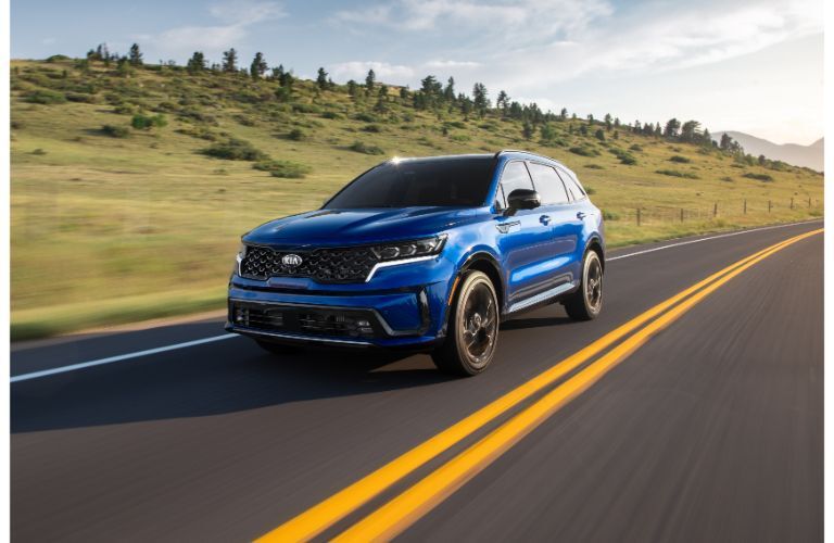 2021 Kia Sorento exterior shot with blue paint color driving down a country highway near hills of trees