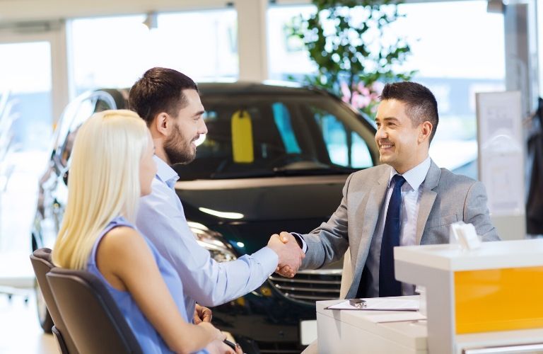 salesman shaking hands with couple in car dealership