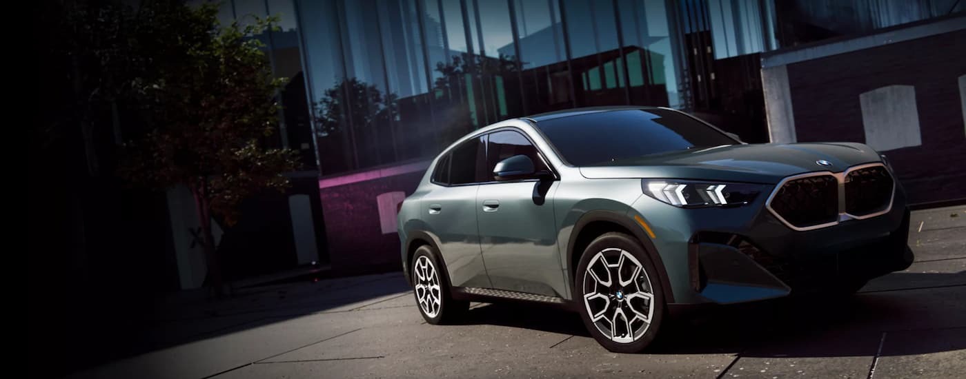 Green 2026 BMW X2 driving on a driveway in front of a building.