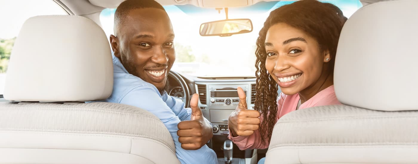 Two people smiling and giving a thumbs up inside of a vehicle.