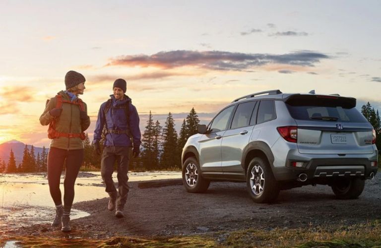 A man and woman walk away after parking the 2023 Honda Passport near a water body