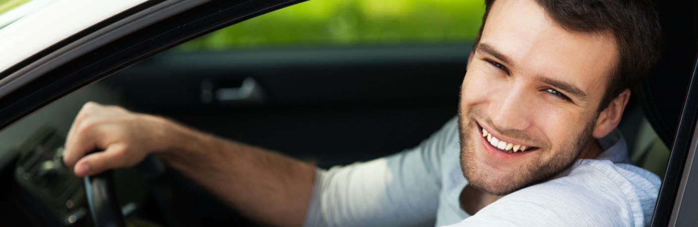 young man driving his car and smiling at the camera