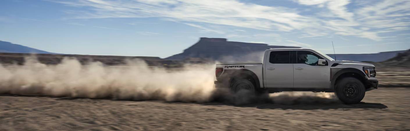 2024 Ford F-150 Raptor side view driving in sand.