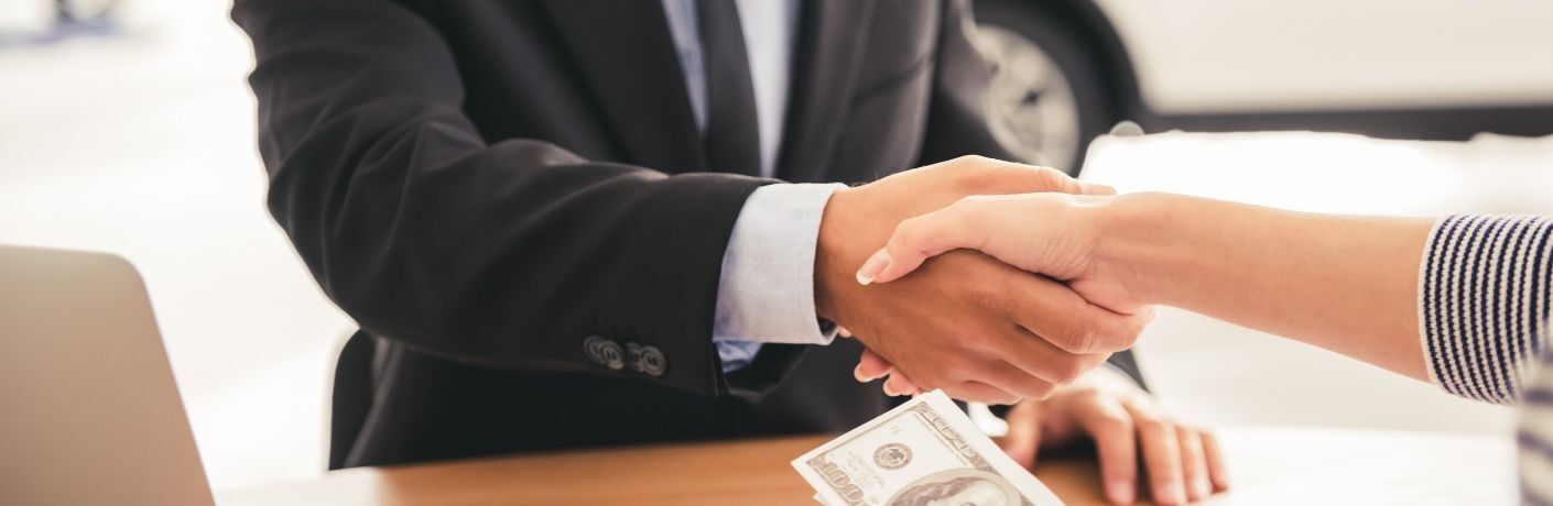 close up of man and woman shaking hands over wood table with money