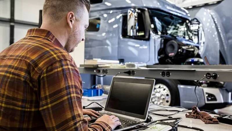A TruckMax commercial truck technician running computer diagnostics on a Volvo commercial truck