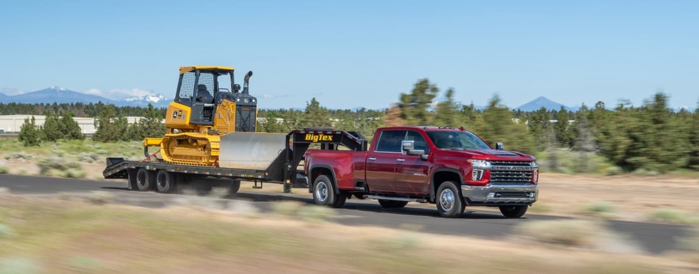 Red 2022 Chevy Silverado 3500 HD towing heavy machinery on a trailer