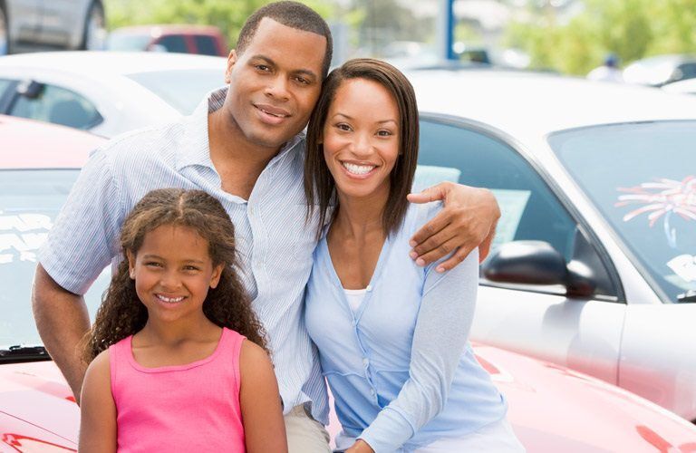 a couple and young girl standing at a dealership