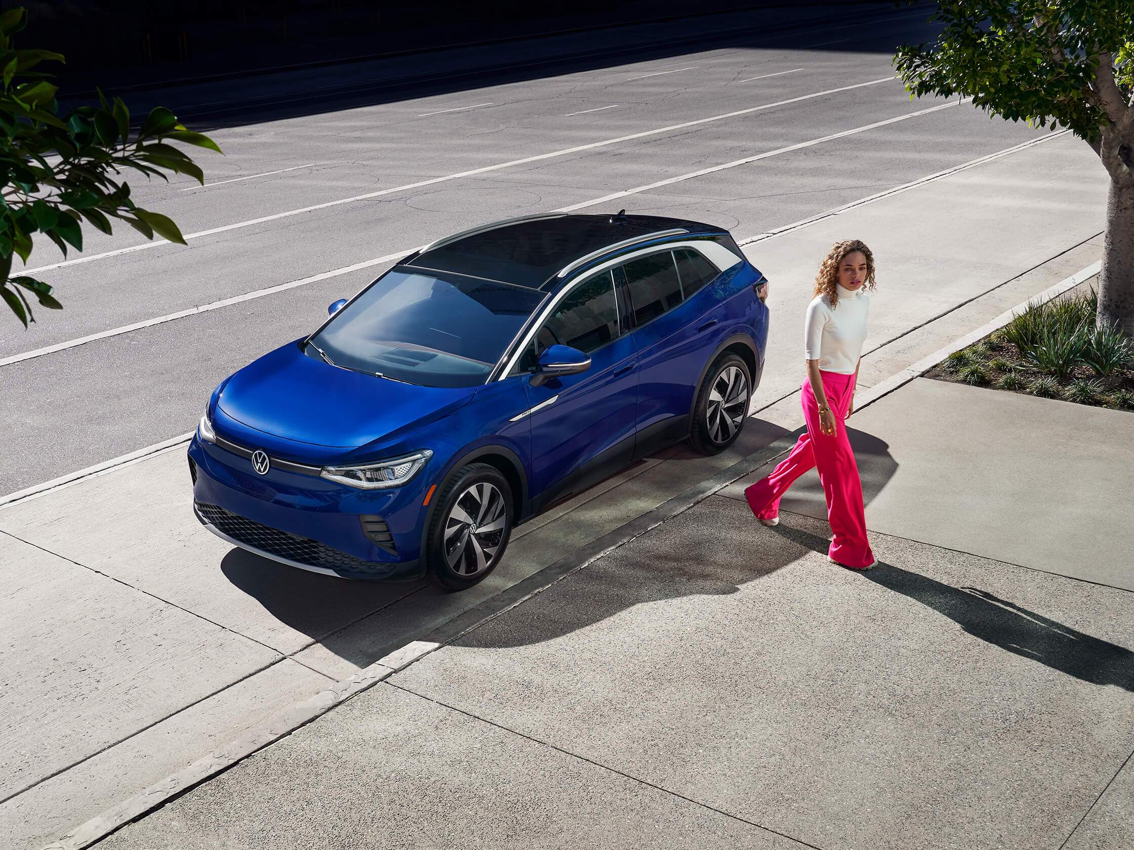 A woman walks away from the driver’s side of an ID.4, shown in Dusk Blue Metallic and parked on a tree-lined street.