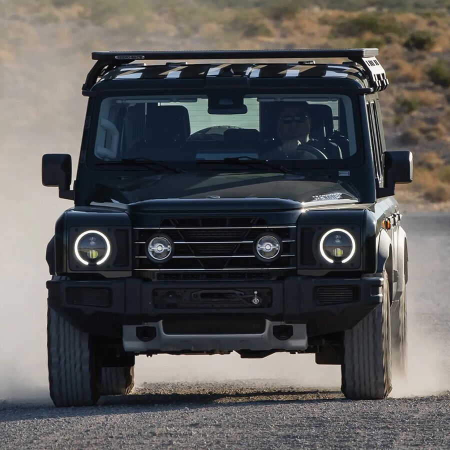 Front view of a 2025 INEOS Grenadier kicking up dust while driving on a desert track.