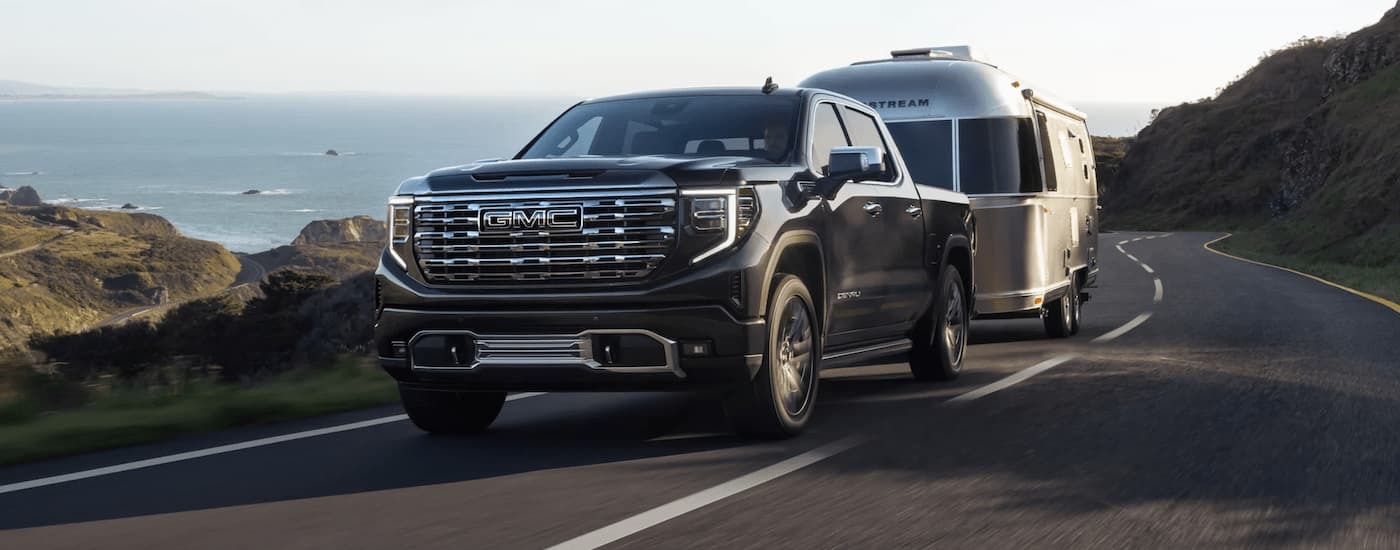 Black 2023 GMC Sierra 1500 Denali towing a silver camper on a winding road