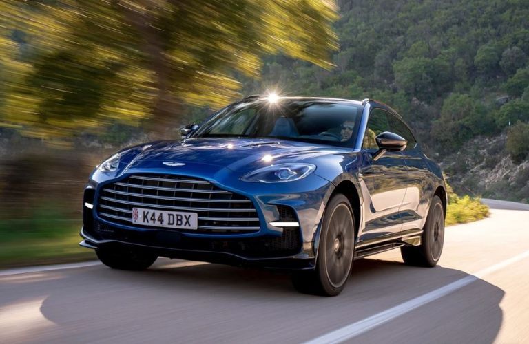 Front view of a blue 2022 Aston Martin DBX SUV driving on a road