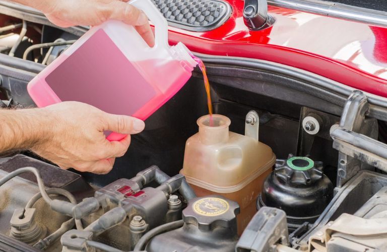 One hand is pouring oil in a car.