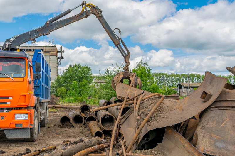 A grapple truck moving heavy pieces of scrap iron.