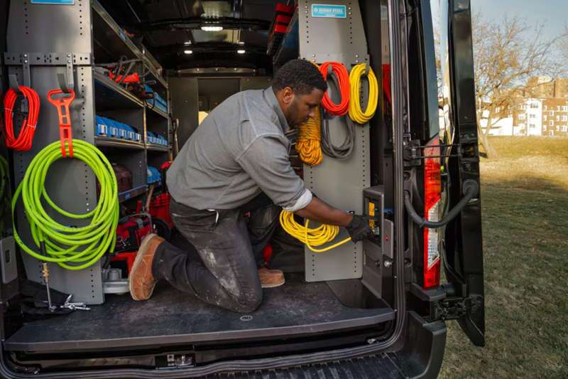 An E-Transit van custom upfitted for an electrician, pictured here plugging into the van's power source