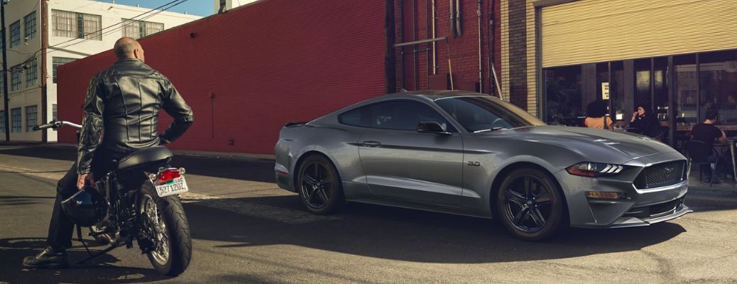 One grey color Ford Mustang is running on the road with a man in bike nearby