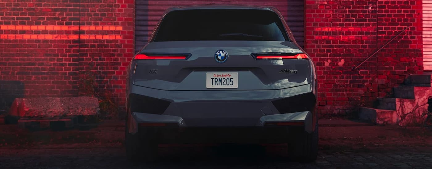 Rear of a grey 2024 BMW iX M60 parked in front of a brick wall.