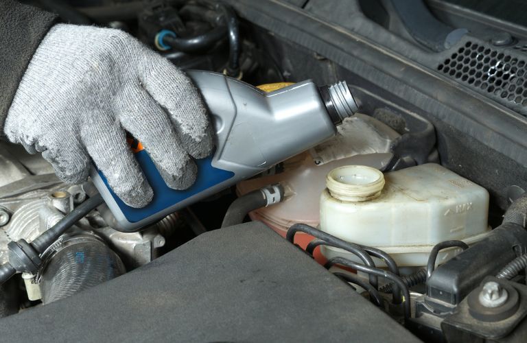 A mechanic's hand pouring brake fluid into an engine