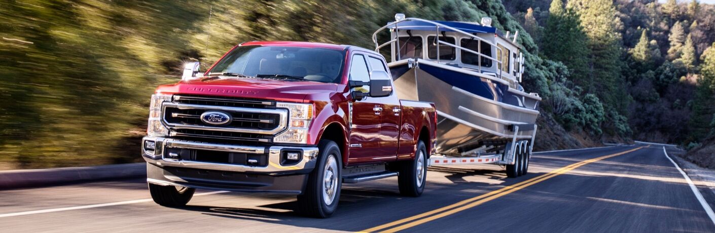 Red 2020 Ford Super Duty towing boat down tree-lined road