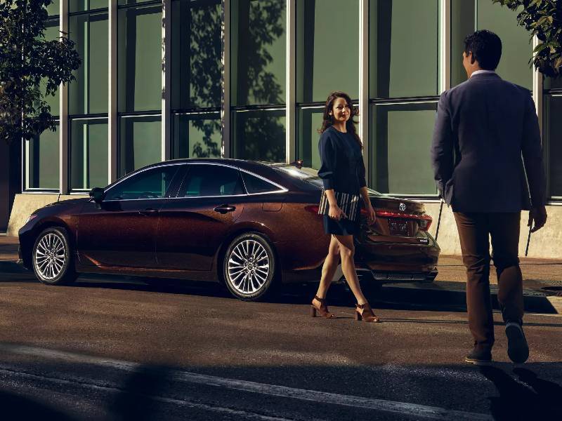 A woman and a man standing near a nice used car on a city street