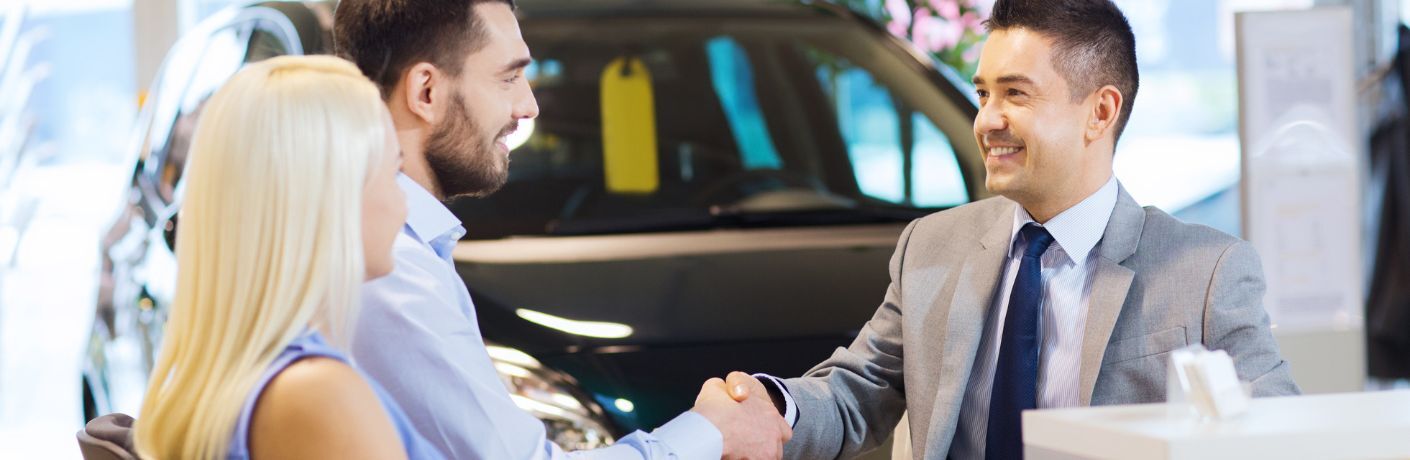 a salesman shaking hand with a couple at a dealership