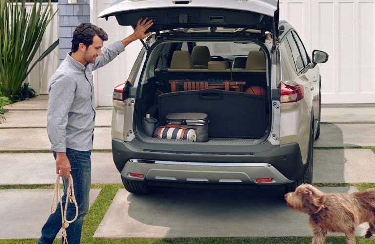 One man is opening the back door of the 2022 Nissan Rogue car and a dog is standing nearby.