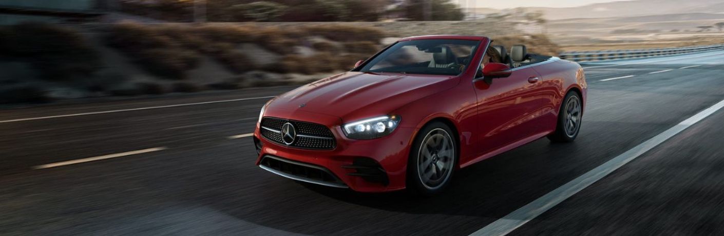 Front quarter view of a red-colored 2022 Mercedes-Benz E-Class Cabriolet driving on a highway.