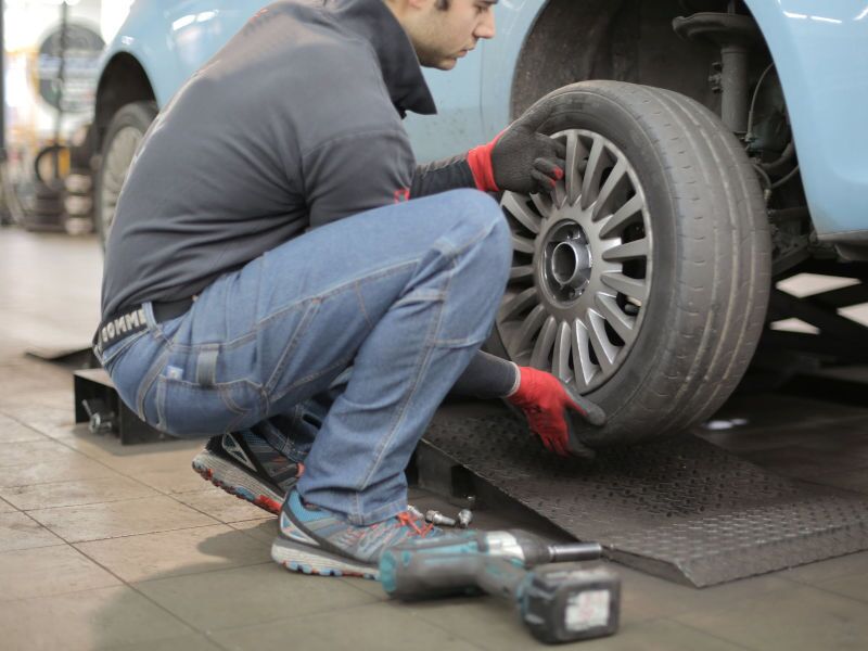 A man removing a wheel to do a tire change on a worn tire.