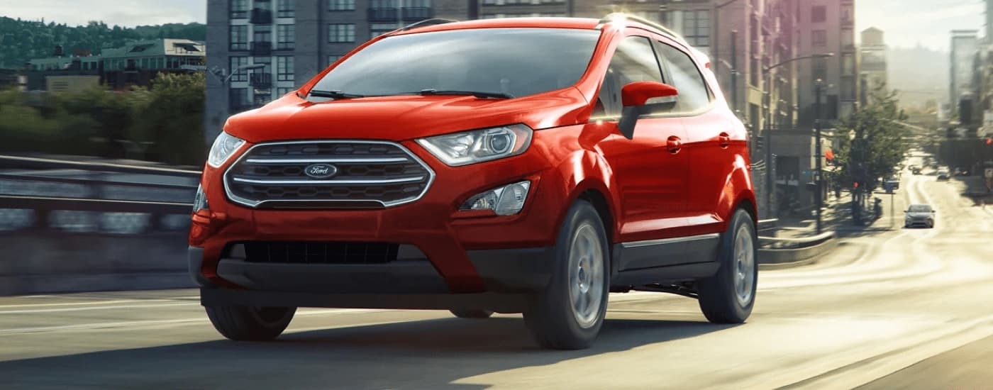 A red 2022 Ford EcoSport SE, a car for sale near Newark, driving on a city street.
