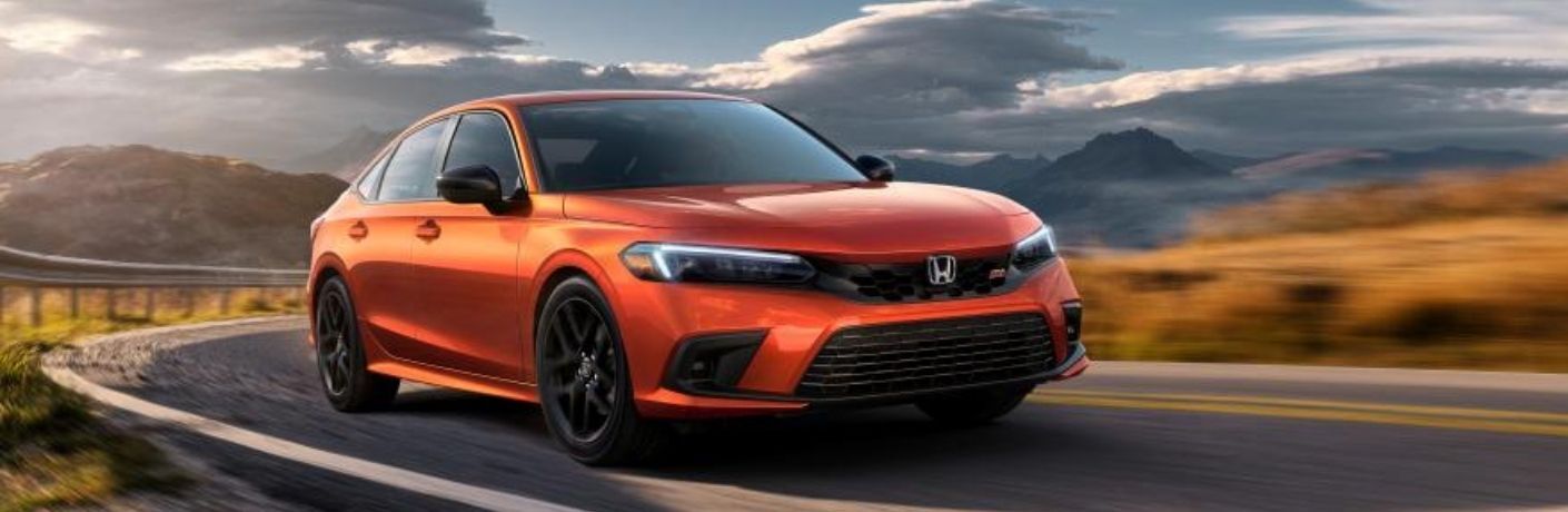 A blazing orange 2022 Honda Civic Si negotiating a corner on a blurred road