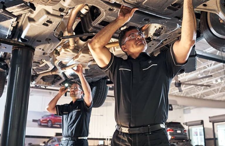 Two mechanics inspecting the underside of a car