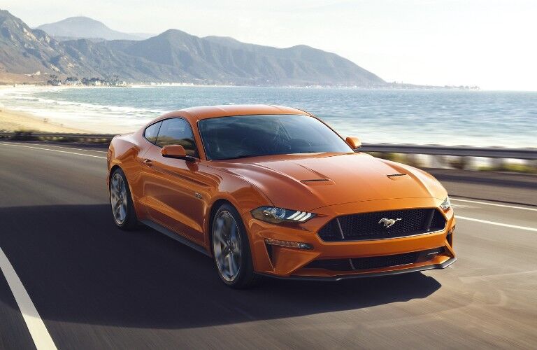 Front passenger angle of an orange 2020 Ford Mustang driving by the ocean
