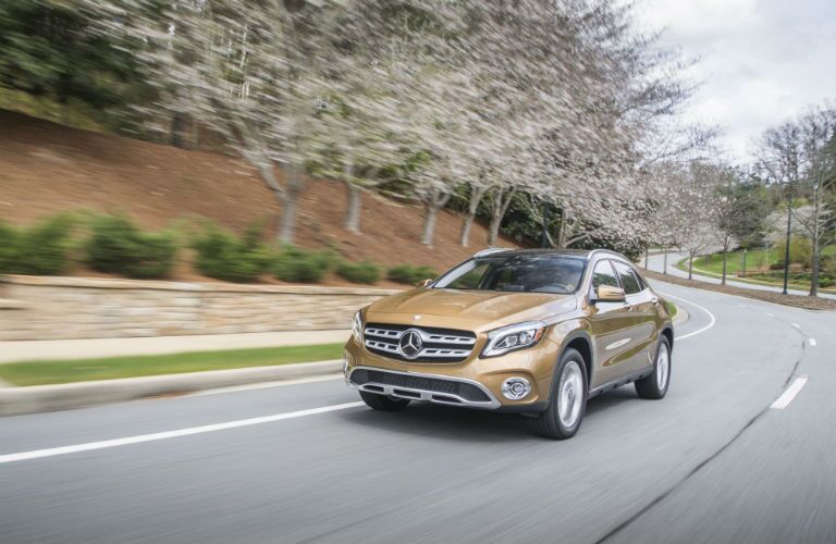 2018 MB GLB exterior front fascia and driver side going fast on winding road with flowering trees