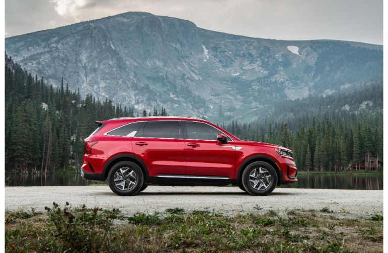 2021 Kia Sorento Hybrid exterior side shot with red paint color parked on a road with a grassy mountain background