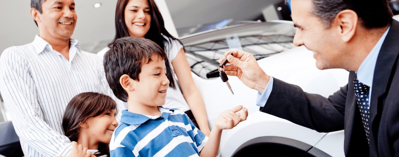 Car salesman handing a key to a family at a dealership.